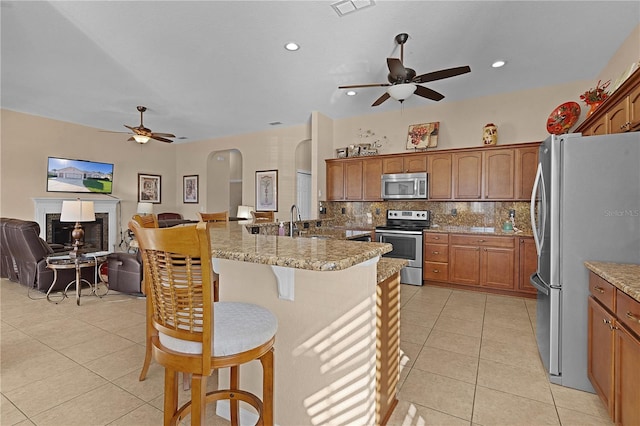 kitchen with a kitchen bar, appliances with stainless steel finishes, backsplash, light stone countertops, and light tile patterned floors