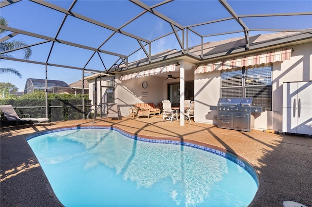 view of pool featuring glass enclosure, ceiling fan, an outdoor kitchen, area for grilling, and a patio