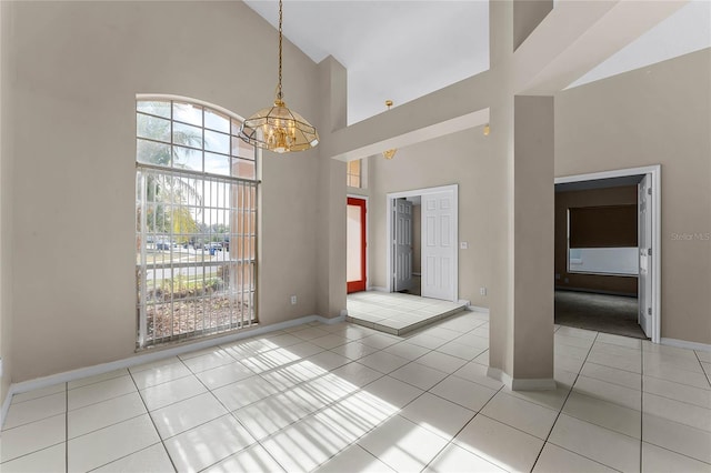 tiled spare room featuring a towering ceiling and an inviting chandelier