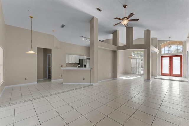 unfurnished living room featuring a towering ceiling, ceiling fan, french doors, and light tile patterned flooring