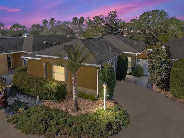 single story home with driveway, roof with shingles, a garage, and stucco siding