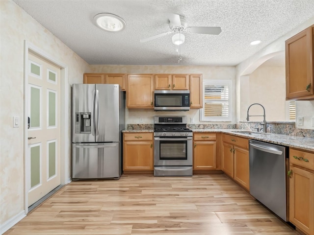 kitchen featuring a textured ceiling, stainless steel appliances, light stone counters, and sink