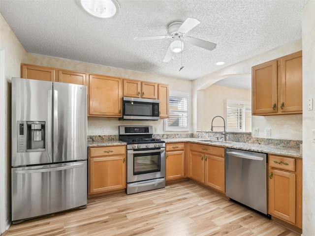 kitchen featuring ceiling fan, sink, light stone counters, and stainless steel appliances