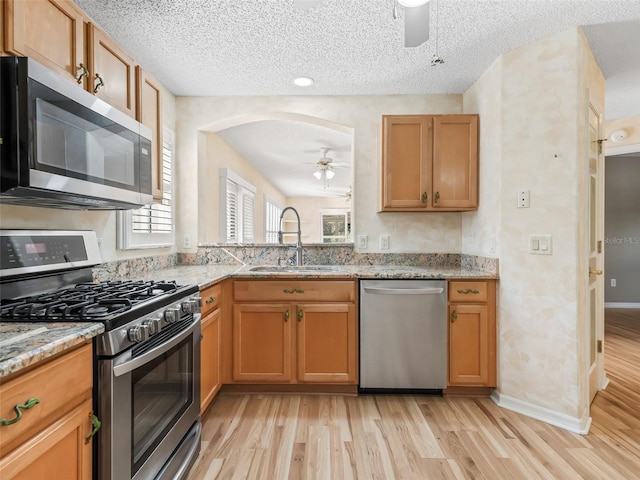 kitchen with light stone countertops, sink, a textured ceiling, appliances with stainless steel finishes, and light wood-type flooring