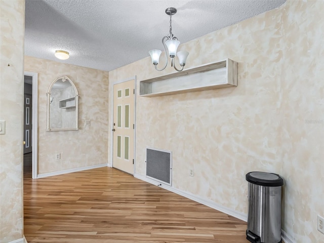 unfurnished dining area featuring wood-type flooring, a textured ceiling, and an inviting chandelier