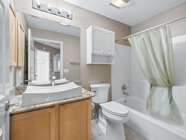 full bathroom with tile patterned floors, vanity, a textured ceiling, shower / tub combo with curtain, and toilet