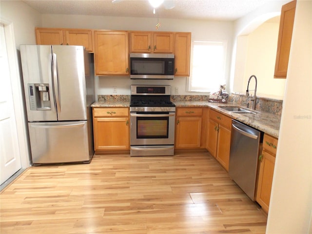 kitchen featuring a textured ceiling, light stone counters, stainless steel appliances, a sink, and light wood-style floors