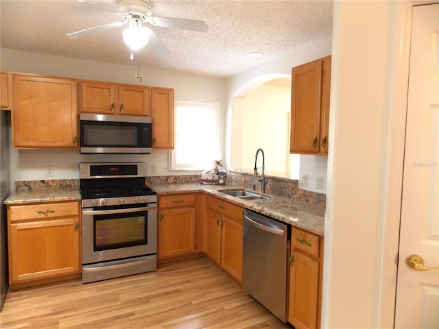 kitchen featuring a textured ceiling, light stone counters, a sink, appliances with stainless steel finishes, and light wood-type flooring