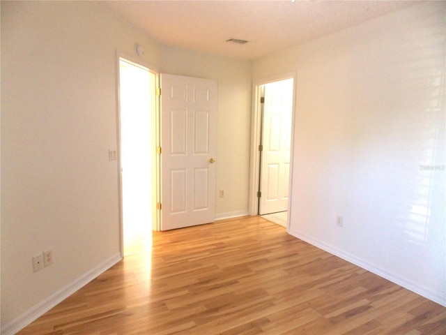 unfurnished room with visible vents, light wood-style flooring, and baseboards