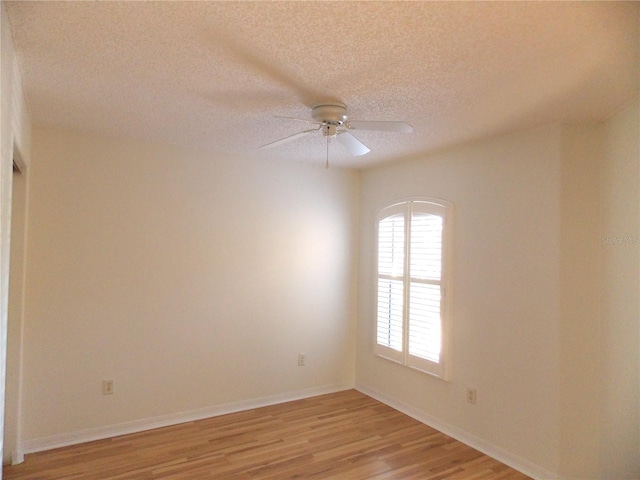 empty room with a textured ceiling, light wood finished floors, a ceiling fan, and baseboards