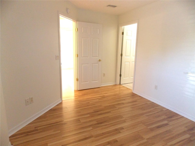 spare room with light wood-type flooring, visible vents, and baseboards