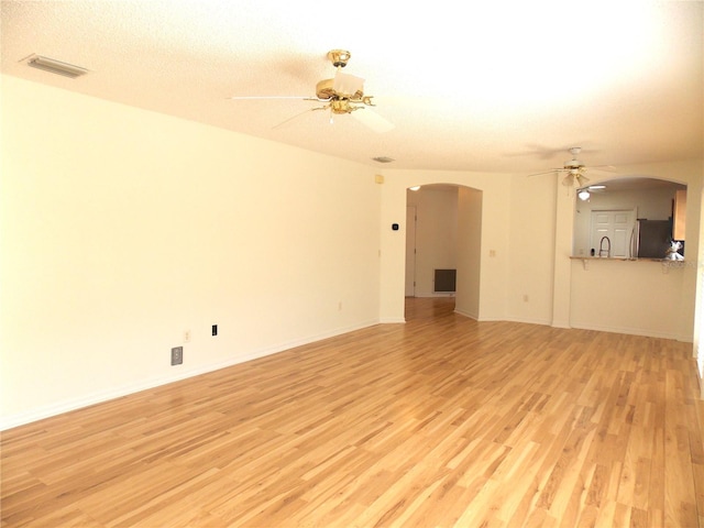 unfurnished living room featuring a ceiling fan, arched walkways, visible vents, and light wood finished floors