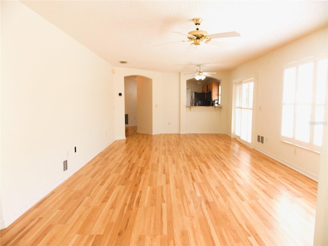 unfurnished living room with arched walkways, ceiling fan, light wood-type flooring, and visible vents