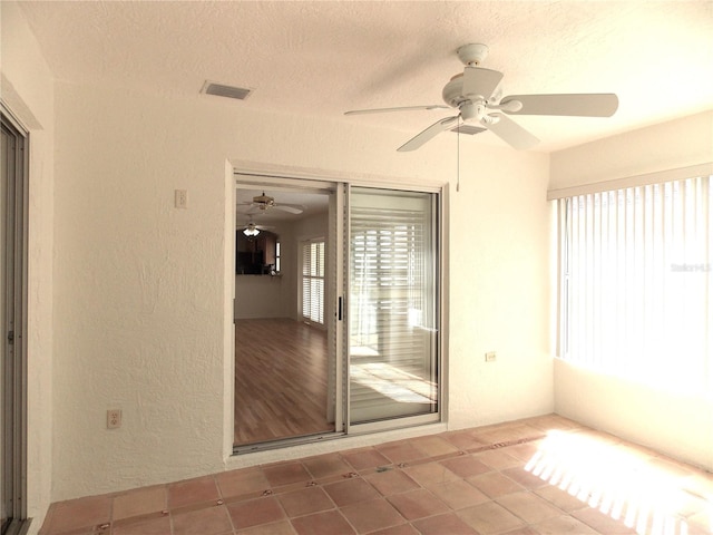 empty room with visible vents, a textured wall, a textured ceiling, and ceiling fan