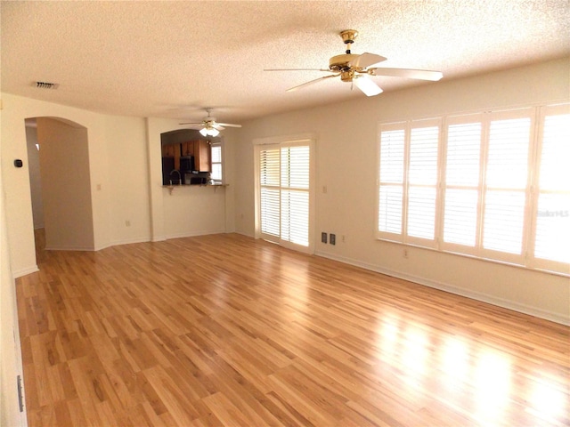 unfurnished living room featuring arched walkways, visible vents, light wood-style flooring, a ceiling fan, and a textured ceiling