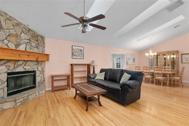 living room with ceiling fan with notable chandelier, light hardwood / wood-style flooring, a stone fireplace, and vaulted ceiling