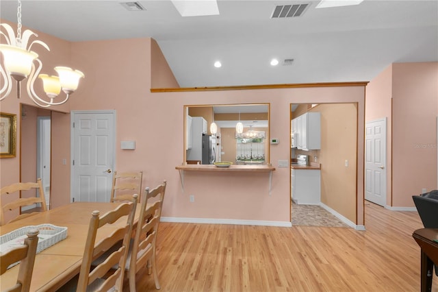 kitchen featuring an inviting chandelier, kitchen peninsula, stainless steel fridge, pendant lighting, and light hardwood / wood-style floors