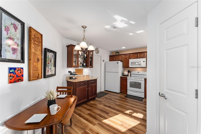 kitchen featuring light stone countertops, dark wood-type flooring, an inviting chandelier, pendant lighting, and white appliances