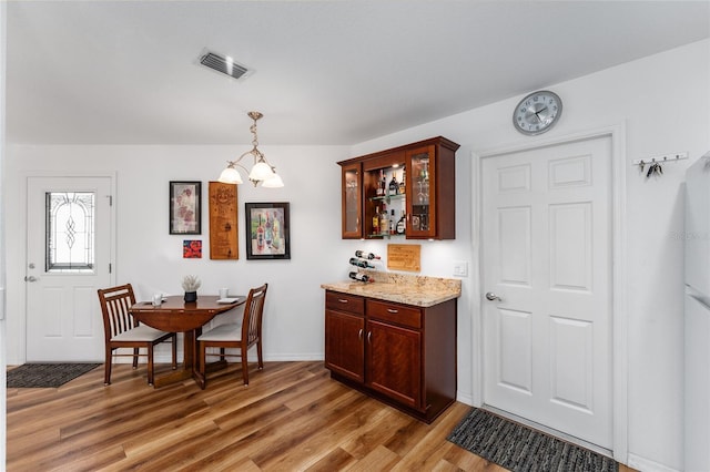 kitchen featuring light stone countertops, dark brown cabinets, hardwood / wood-style flooring, a notable chandelier, and hanging light fixtures