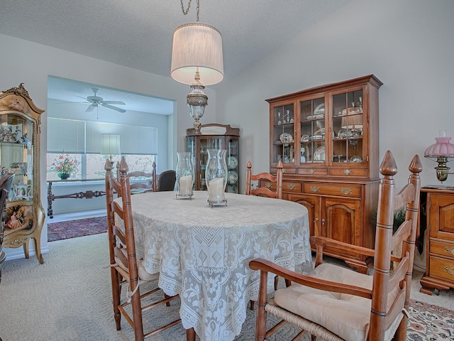 dining space featuring vaulted ceiling, light colored carpet, ceiling fan, and a textured ceiling