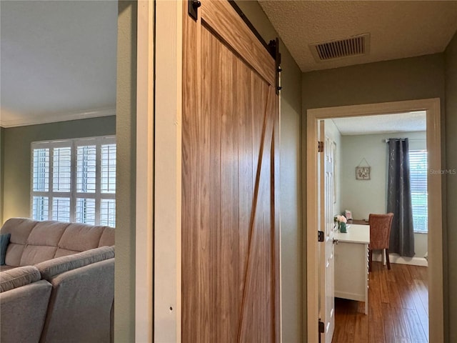 hall with wood-type flooring, a wealth of natural light, a barn door, and a textured ceiling