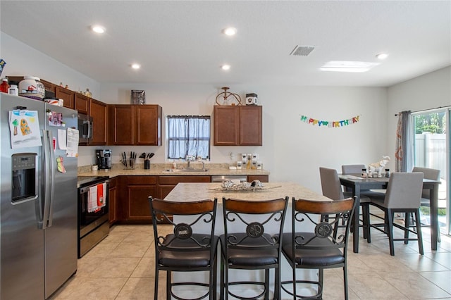 kitchen with a center island, a kitchen breakfast bar, sink, light tile patterned floors, and stainless steel appliances