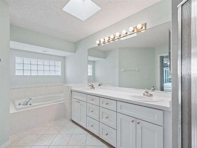 bathroom with a skylight, tile patterned flooring, tiled bath, a textured ceiling, and vanity