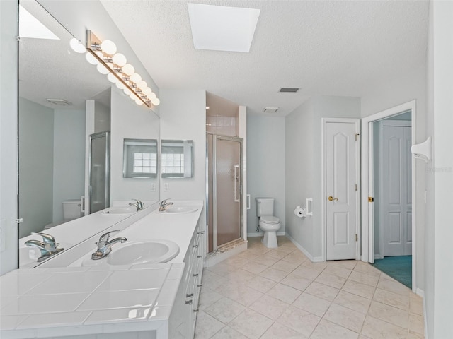 bathroom featuring a textured ceiling, a skylight, toilet, and a shower with shower door