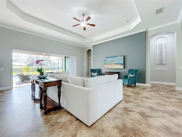 living room featuring a raised ceiling, ceiling fan, and ornamental molding