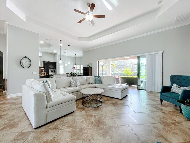 living room featuring a raised ceiling, ceiling fan, and ornamental molding