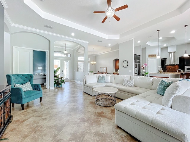 living room featuring a tray ceiling, crown molding, french doors, and ceiling fan with notable chandelier