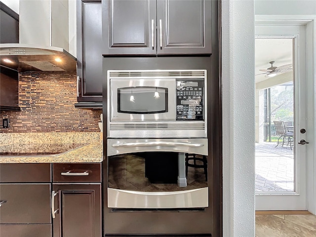 kitchen featuring appliances with stainless steel finishes, light stone counters, dark brown cabinets, and wall chimney range hood