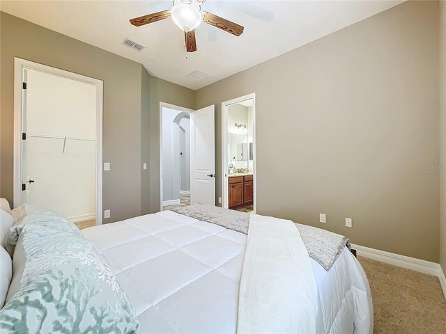 carpeted bedroom featuring a walk in closet, a closet, ensuite bathroom, and ceiling fan