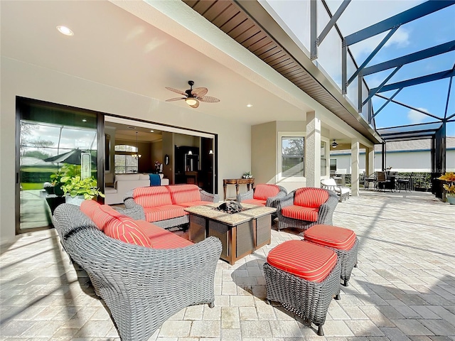 view of patio with a lanai, ceiling fan, and an outdoor living space with a fire pit