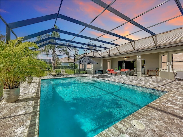 pool at dusk with glass enclosure, outdoor lounge area, and a patio