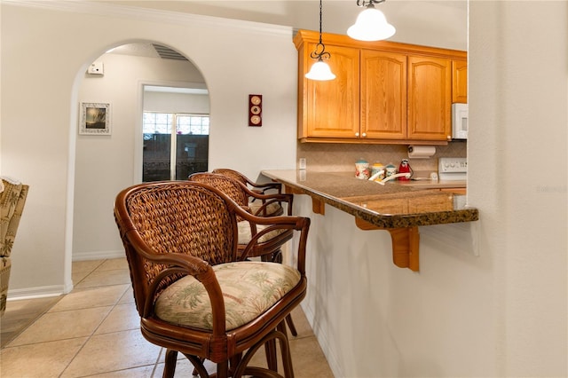 kitchen featuring decorative backsplash, a kitchen bar, crown molding, light tile patterned floors, and decorative light fixtures