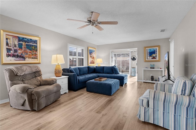 living room featuring ceiling fan, light hardwood / wood-style flooring, and a textured ceiling