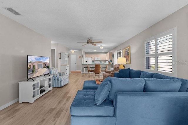 living room with ceiling fan, a textured ceiling, and light hardwood / wood-style floors