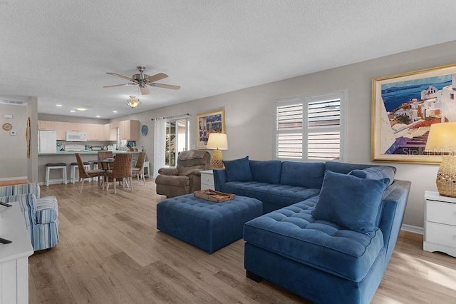 living room with ceiling fan, light hardwood / wood-style floors, and a textured ceiling