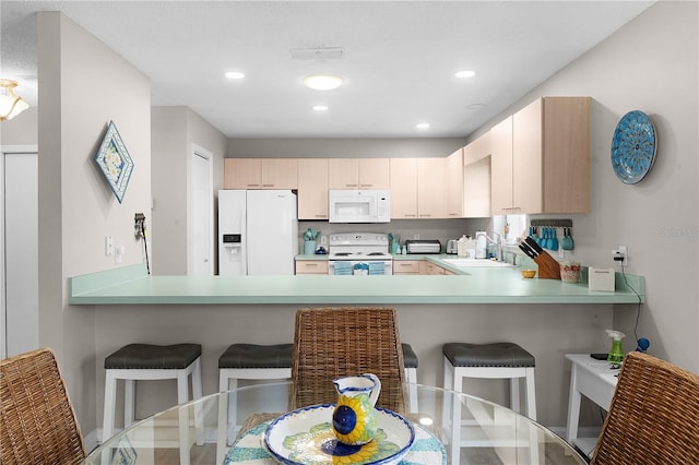 kitchen with a kitchen bar, sink, light brown cabinets, kitchen peninsula, and white appliances