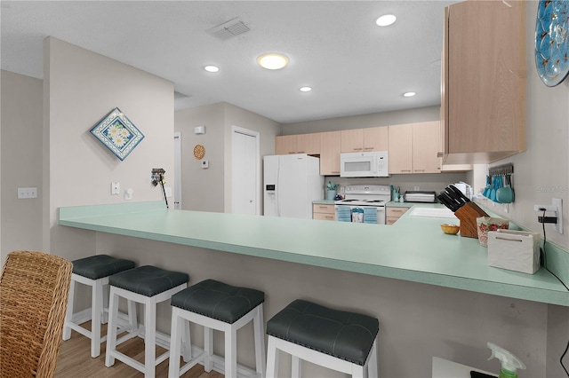 kitchen featuring light brown cabinetry, white appliances, a breakfast bar area, and kitchen peninsula