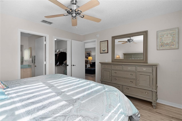 bedroom featuring ensuite bathroom, a spacious closet, ceiling fan, a textured ceiling, and light hardwood / wood-style flooring