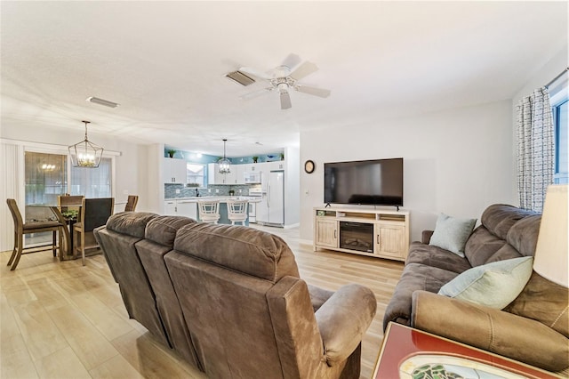 living room featuring ceiling fan with notable chandelier and light wood-type flooring