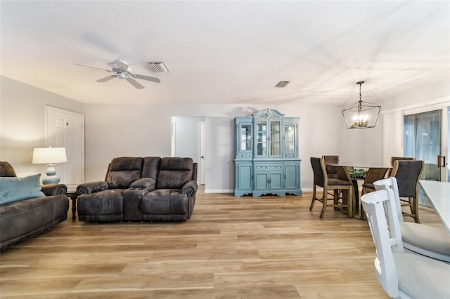 living room featuring ceiling fan with notable chandelier, a textured ceiling, and light wood-type flooring