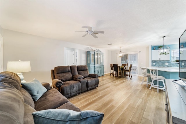 living room featuring ceiling fan with notable chandelier and light hardwood / wood-style flooring