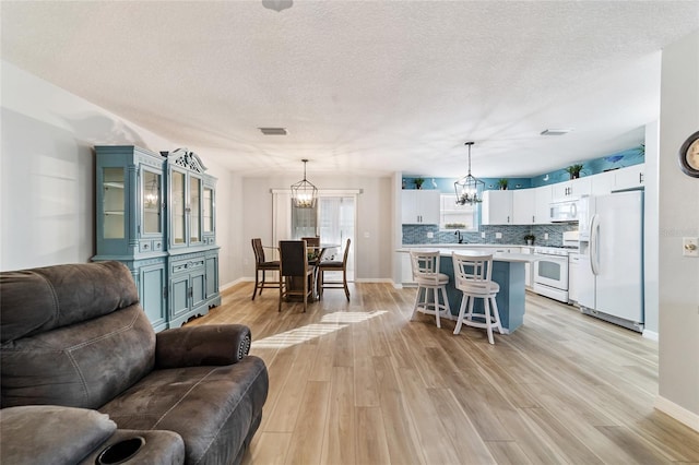 living room with sink, light hardwood / wood-style floors, a textured ceiling, and a notable chandelier