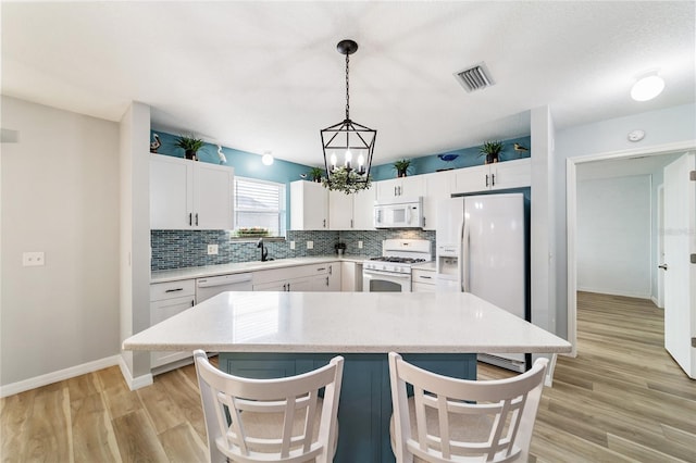 kitchen with pendant lighting, white appliances, white cabinetry, and a kitchen island