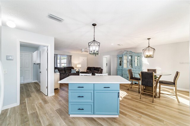 kitchen featuring light wood-type flooring, ceiling fan with notable chandelier, blue cabinets, a center island, and hanging light fixtures