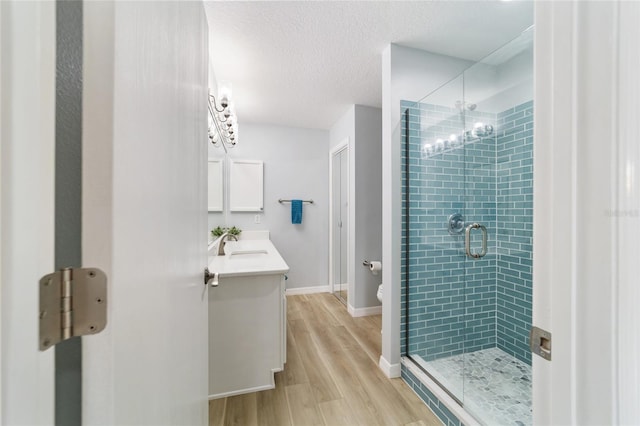 bathroom with a textured ceiling, toilet, vanity, a shower with shower door, and hardwood / wood-style flooring