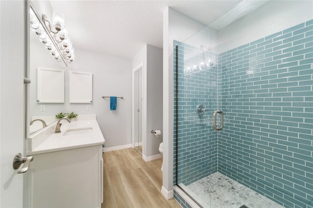 bathroom featuring vanity, hardwood / wood-style flooring, toilet, walk in shower, and a textured ceiling